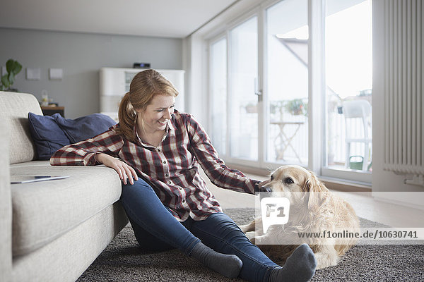 Smiling young woman sitting beside her dog on the floor at home