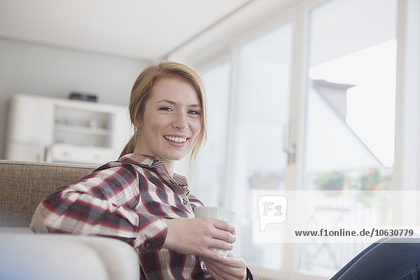 Porträt einer lächelnden jungen Frau bei einer Tasse Kaffee zu Hause