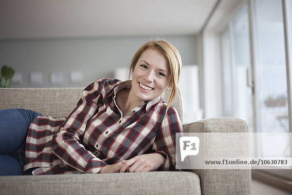 Porträt einer lächelnden jungen Frau  die zu Hause auf der Couch liegt.