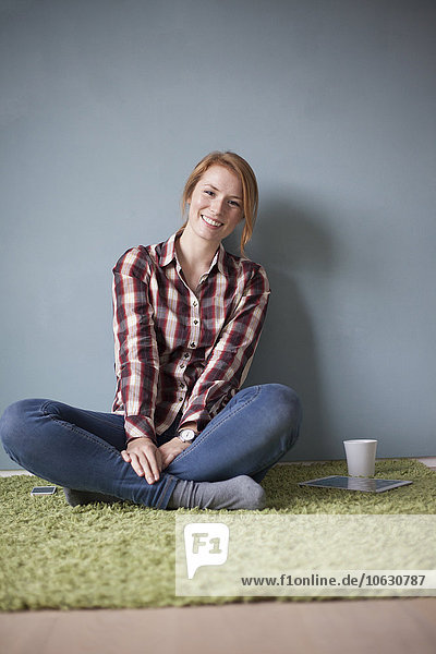 Porträt einer lächelnden jungen Frau auf dem Boden sitzend
