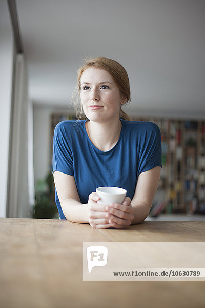 Portrait of young woman sitting at table with cup of coffee