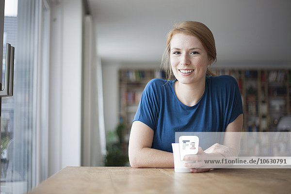 Portrait of smiling young woman sitting at table with cup of coffee