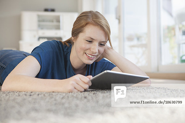 Porträt einer lächelnden jungen Frau mit digitalem Tablett zum Entspannen auf dem Boden zu Hause