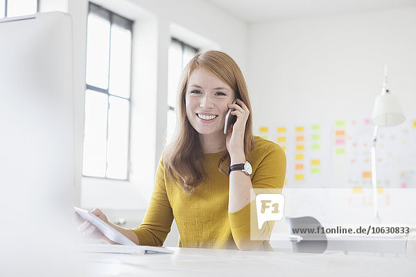 Junge Frau im Büro arbeitet am Schreibtisch mit Smartphone