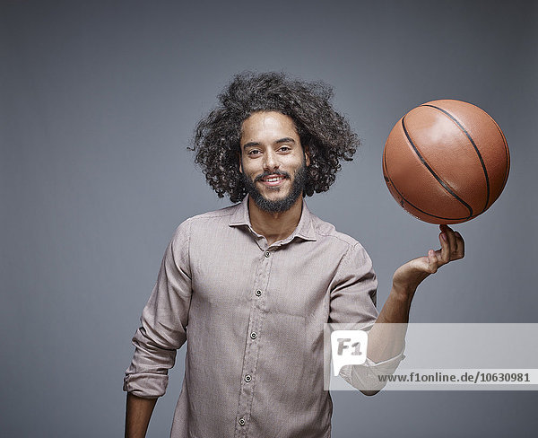 Portrait of smiling young man with curly brown hair balancing a basketball on his finger