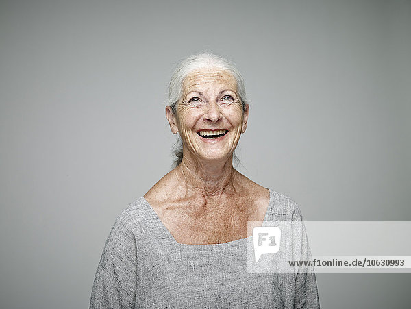 Porträt einer lachenden Seniorin  die vor grauem Hintergrund aufblickt