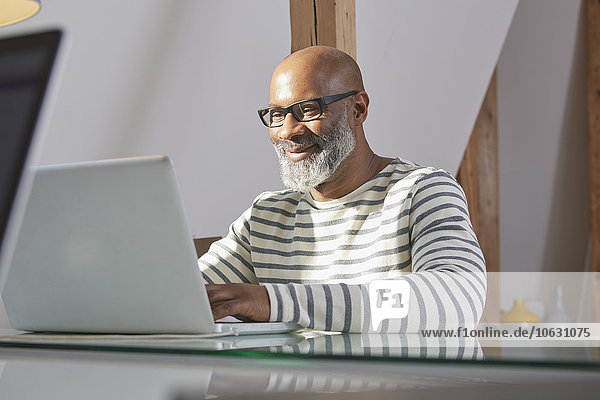 Portrait eines lächelnden Mannes  der am Schreibtisch sitzt und mit dem Laptop arbeitet.
