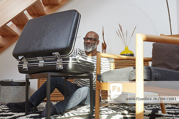 Smiling man sitting on the floor of his living room packing suitcase