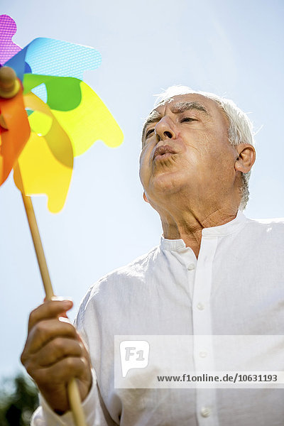 Senior man blowing against pinwheel outdoors