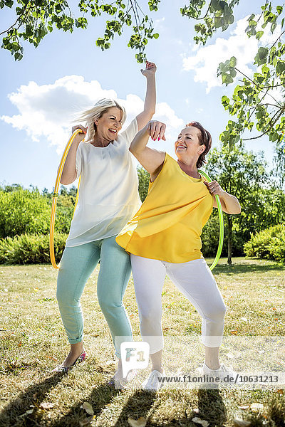 Happy mature women with hula hoops on meadow