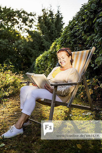 Smiling mature woman reading book in deck chair in garden