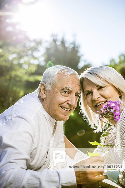 Smiling elderly couple with flower in garden