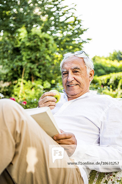 Lächelnder älterer Mann liest Buch im Garten