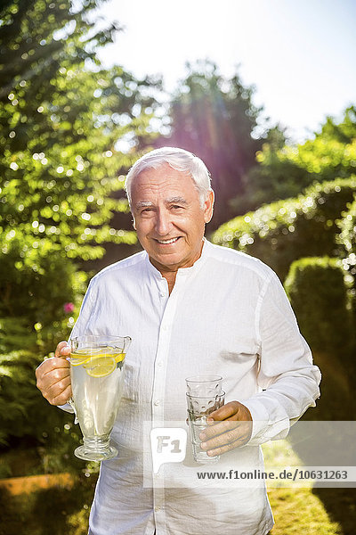 Lächelnder älterer Mann mit Wasserkaraffe im Garten