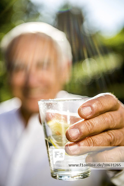 Nahaufnahme eines älteren Mannes,  der ein Glas Wasser hält.