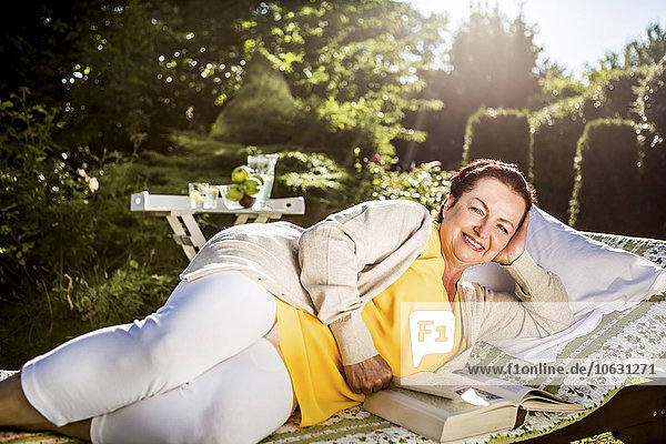 Smiling mature woman reading book on garden lounge