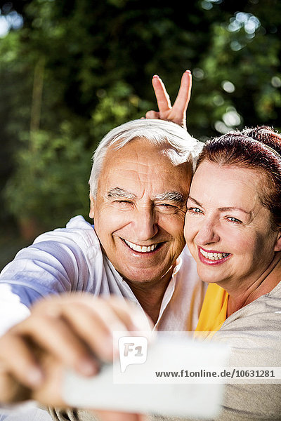 Verspieltes älteres Paar mit einem Selfie im Freien