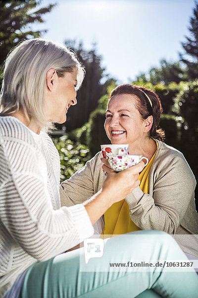 Glückliche reife Frauen im Garten mit Kaffeetassen