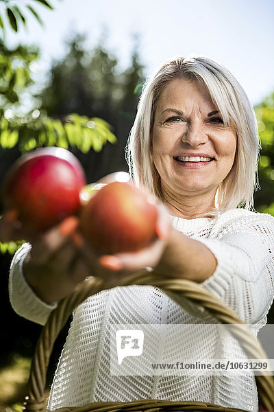 Lächelnde reife Frau mit Äpfeln im Freien