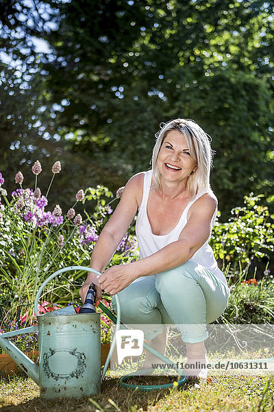 Smiling mature woman with hose and watering can in garden