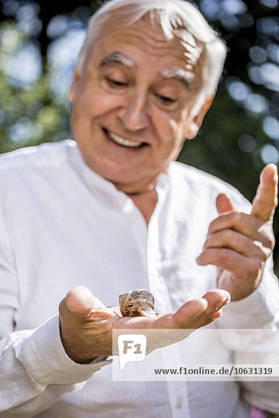Smiling senior man with snail in his hand