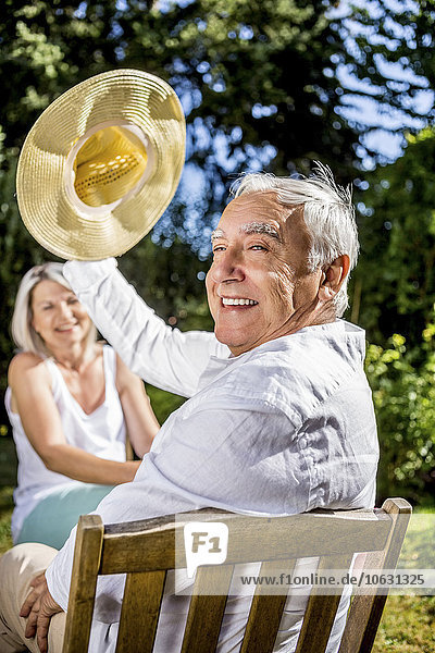Glücklicher älterer Mann im Garten mit Frau im Hintergrund