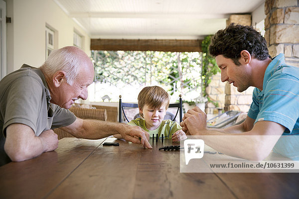 Kleiner Junge spielt mit seinem Vater und Großvater Domino