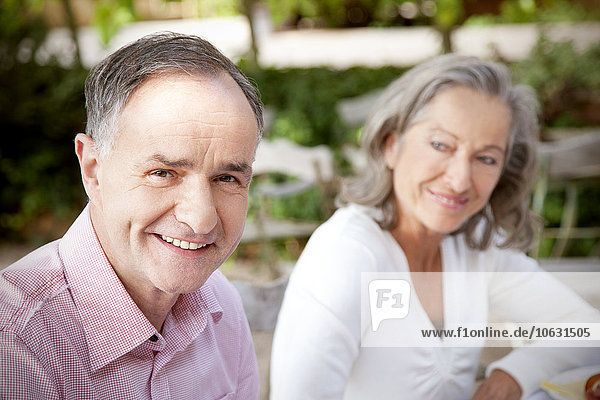 Porträt des lächelnden reifen Mannes und der Frau im Hintergrund im Garten