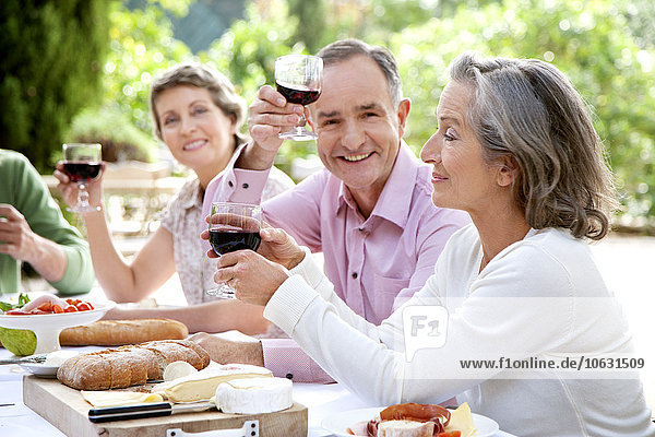 Spanien  Mallorca  reifer Mann sitzend mit Freunden am gedeckten Tisch im Garten  Toast mit Rotwein