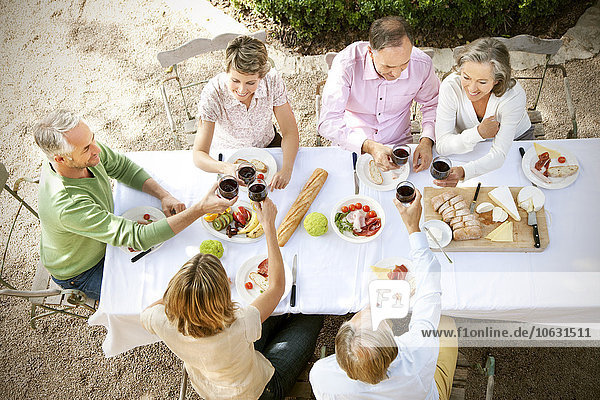 Spain  Mallorca  six friends sitting at laid table in the garden toasting with red wine