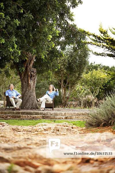 Spanien  Mallorca  Paare  die sich unter einem Baum in ihrem Garten entspannen.