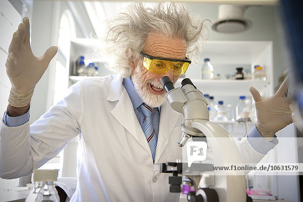 Tousled professor examining samples under microscope  looking surprised