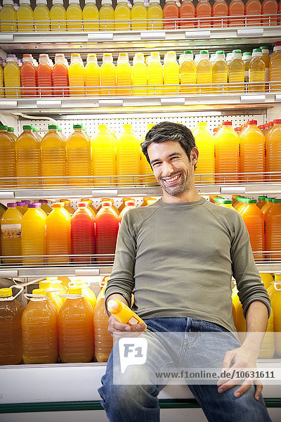 Porträt eines lächelnden Mannes vor dem Kühlschrank mit Reihen von Saftflaschen in einem Supermarkt.