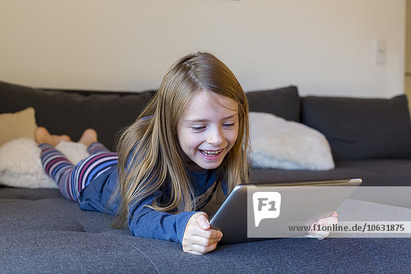 Smiling girl lying on the couch using digital tablet