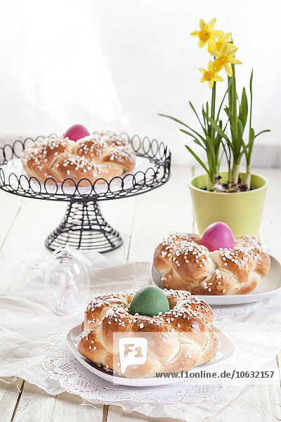 Geflochtenes Osterbrot mit bunten Eiern und Narzisse