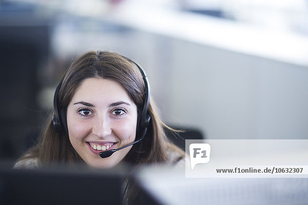 Porträt einer lächelnden jungen Frau mit Kopfhörer am Arbeitsplatz