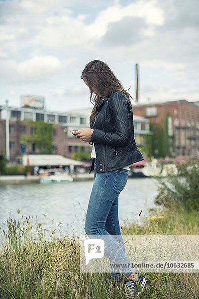 Deutschland  Münster  junge Frau auf einer Wiese am Stadthafen mit Blick auf ihr Smartphone