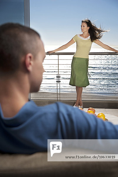 Junger Mann auf Couch mit Freundin auf dem Balkon am Meer stehend
