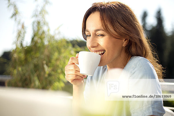 Glückliche Frau auf dem Balkon mit Tasse Kaffee und Laptop