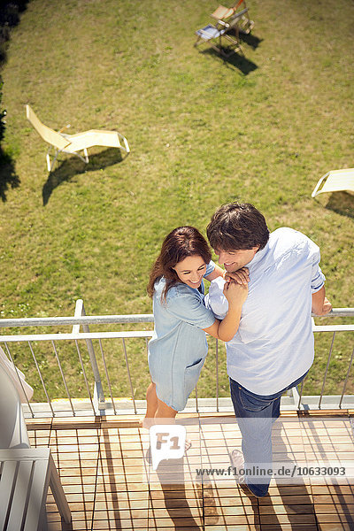 Happy couple standing on balcony above garden