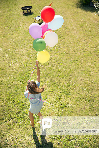 Frau steht im Garten und hält bunte Luftballons.