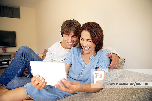 Happy couple relaxing on couch looking at digital tablet