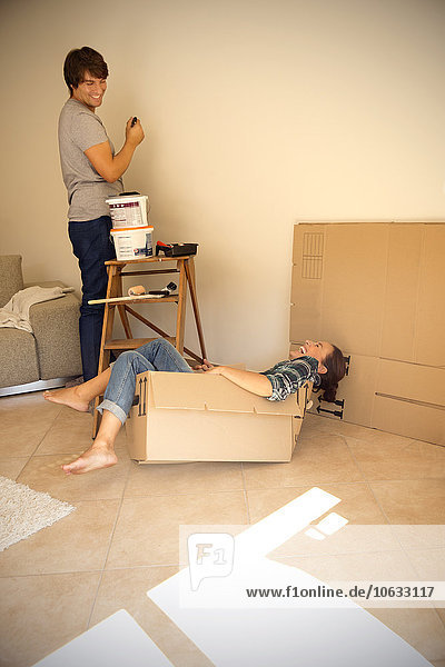 Laughing woman in cardboard box with man painting wall