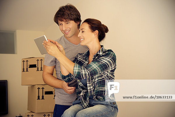 Lächelndes Paar beim Betrachten des digitalen Tabletts mit Kartonschachteln im Hintergrund