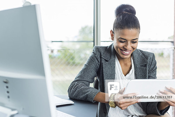 Lächelnde junge Frau im Büro sucht auf digitalem Tablett
