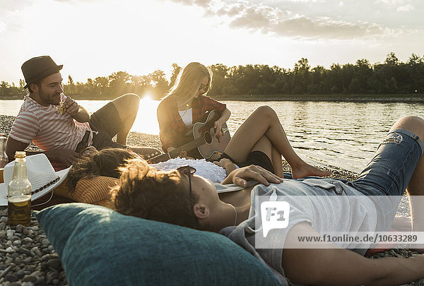 Freunde beim Sonnenuntergang am Flussufer entspannen