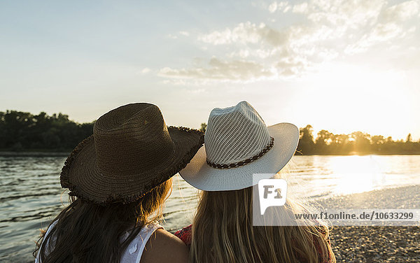 Two friends wearing straw hats relaxing at the riverside at sunset
