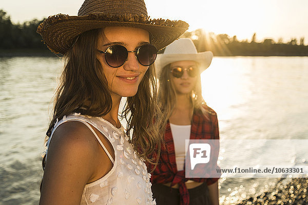 Two friends wearing straw hats and sunglasses at the riverside at sunset