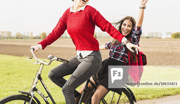 Two exuberant young women sharing a bicycle in rural landscape