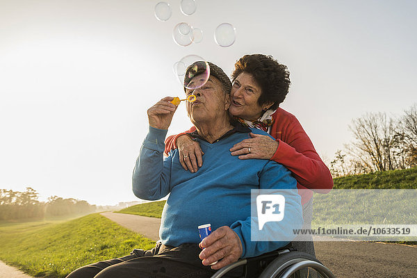 Senior woman with husband in wheelchair blowing soap bubbles